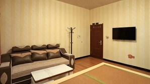 A room with a sofa, a flat-screen TV, a wooden floor, and a door. - Dasheng Chinese Inn (Wusong Island Scenic Area) (Jilin City)