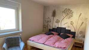 Un dormitorio con cama de madera, ropa de cama a cuadros, una silla, una mesita de noche y un mural en la pared.