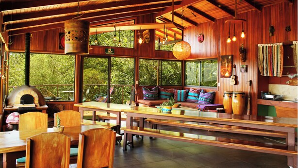 Un interior rústico de madera con una gran mesa de comedor, bancos y un rincón de estar acogedor con cojines.