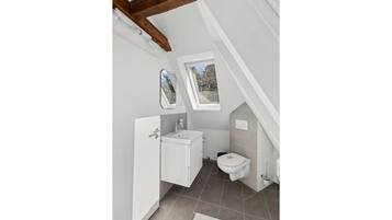 Une petite salle de bain blanche, avec une fenêtre, un lavabo et des toilettes.