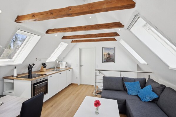 Um apartamento moderno no estilo loft, com cozinha, área de refeições e sala de estar. Possui vigas de madeira aparentes, claraboias e uma escada.