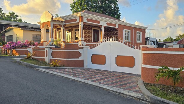 Ein zweistöckiges Haus mit befestigtem Eingangsbereich, einem Pflasterweg und einem kleinen Garten mit blühenden Pflanzen.