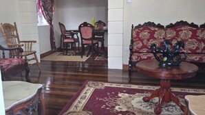 Ein Essbereich mit einem Holztisch und Stühlen, einem gemusterten Teppich und einem Sofa mit Blumenmuster.