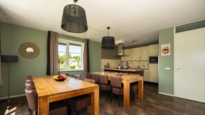 Uma cozinha moderna com uma ilha central, uma área de jantar com mesa e cadeiras de madeira, e vista para o exterior através de uma janela.