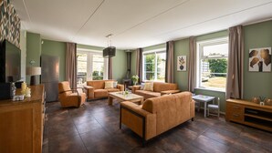 Uma sala de estar espaçosa com sofás, uma mesa de centro e uma televisão. Há janelas com cortinas, uma lareira e um armário de madeira.