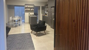 A modern kitchen with grey cabinets, a black refrigerator, and a dining area with a black sofa and white chairs. - GEMINADO CASA 4 ALTO PADR ÃO 3 QUARTOS (Joinville)