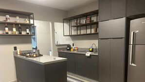 A modern kitchen with a central island, dark cabinetry, and a stainless steel refrigerator. - GEMINADO CASA 4 ALTO PADRÃO 3 QUARTOS (Joinville)