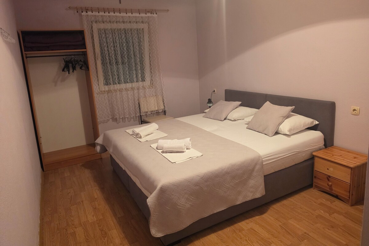 A bedroom with a bed, nightstand, and a window with a curtain.
