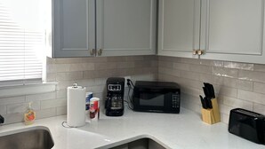 A kitchen with grey cabinets, a coffee maker, a microwave, a toaster, and a sink. - Suite A at Blue Sky Terrace (Columbus)