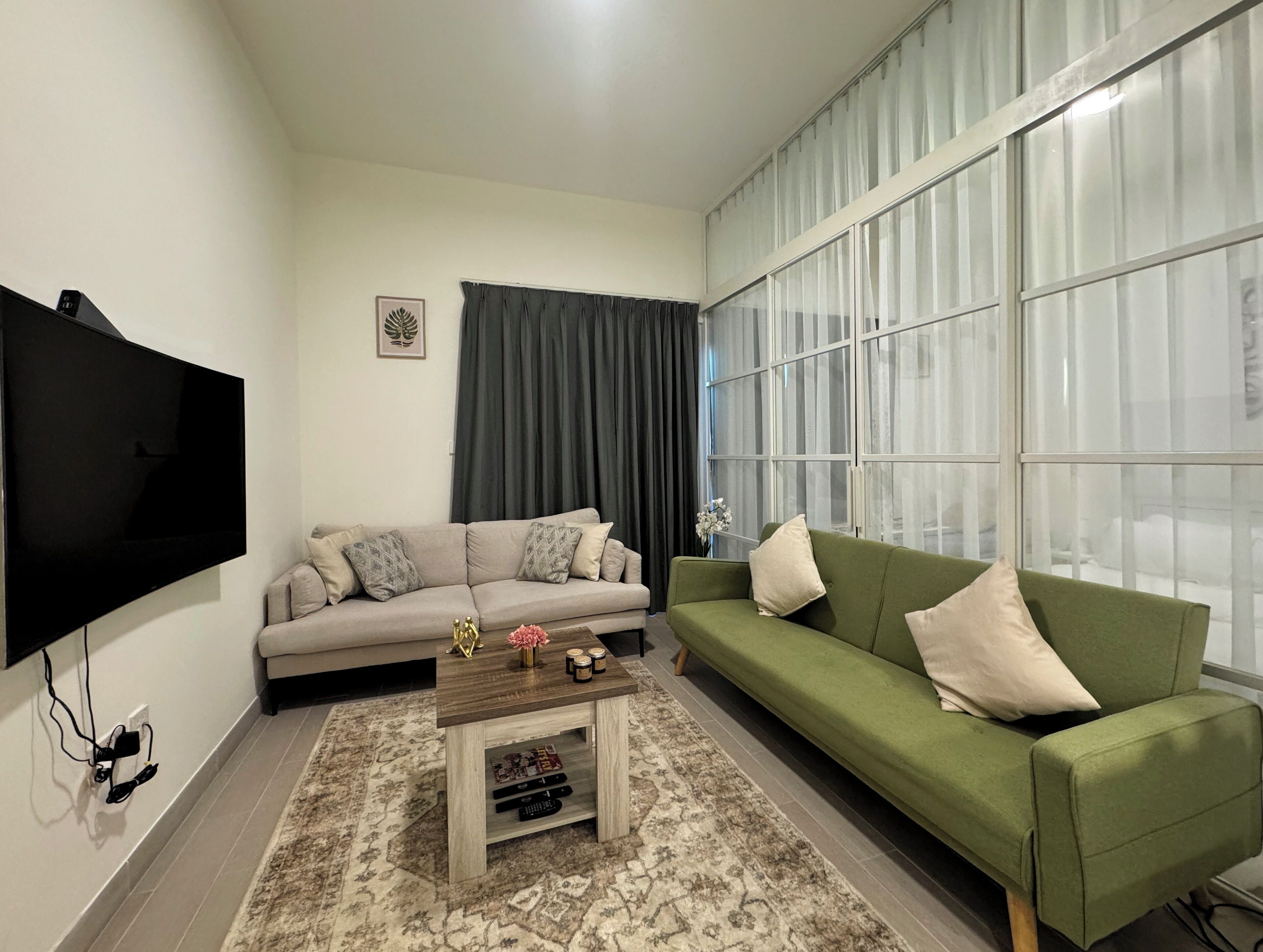 A living room with a flat-screen TV, two sofas, a coffee table, and a large window with curtains.