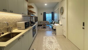 Een moderne keuken met inbouwapparatuur, een zithoek met een bank en tafel, en uitzicht op de stad door grote ramen.