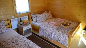 Una habitación acogedora tipo cabaña de madera con dos camas, una mesita con una cesta de fruta y una botella, y una ventana con cortina.