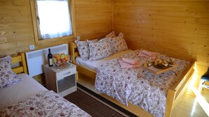 A cozy wooden cabin room with two beds, a small table with a bottle and fruit, and a window with curtains.