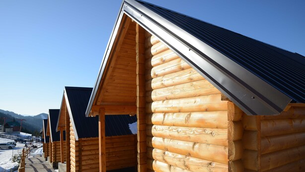 A row of log cabins with pitched roofs, wooden walls, and a clear sky in the background.