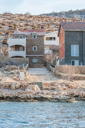 Situated on a rocky terrain, this coastal property offers a blend of traditional and modern architecture with a stone pathway leading to the entrance.