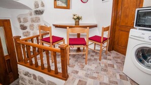 Une cuisine compacte avec un mur en pierre, une table en bois avec des chaises, un lave-linge et une horloge au mur.