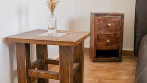 A small wooden table with a vase of dried flowers on top, positioned next to a wooden nightstand with a drawer.