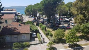 A coastal residential area with parked cars, trees, and buildings with red-tiled roofs. - Relaxing Tivat Stay with Balcony -Two Bedroom Apt (Tivat)