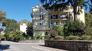 A multi-story building with balconies, surrounded by greenery and a stone wall. - Relaxing Tivat Stay with Balcony -Two Bedroom Apt (Tivat)