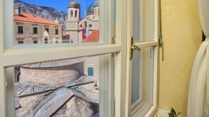 Una habitación con ventana que da a un edificio histórico con techos en cúpula y montañas al fondo.