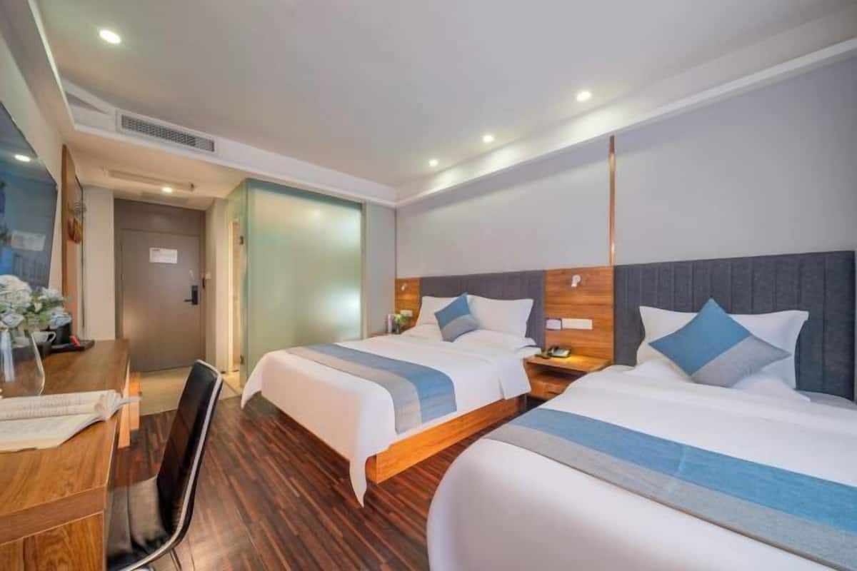 A hotel room with two beds, a wooden desk, and a chair.