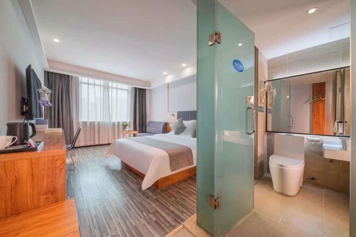 A modern hotel room with a bed, a desk, a shower, and a bathroom.