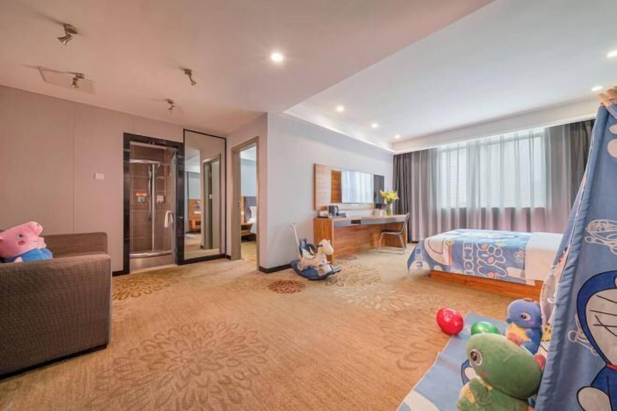 A hotel room with a bed, a desk, a chair, a sofa, a mirror, and a door.
