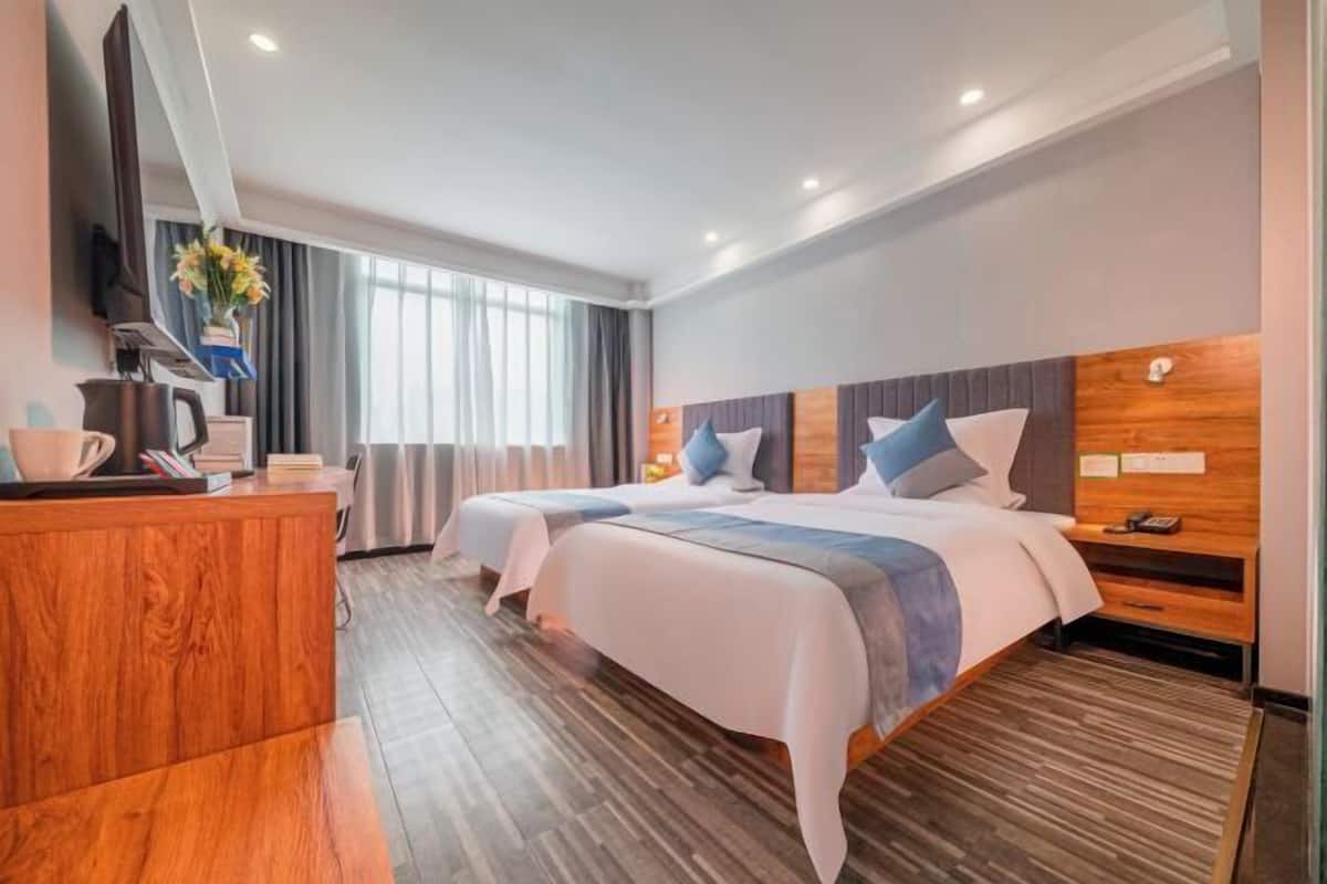 A hotel room with two beds, a wooden desk, a TV, and a window with curtains.