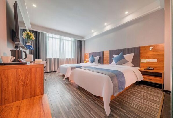 Een hotelkamer met twee bedden, een houten bureau, een televisie en een raam met gordijnen.