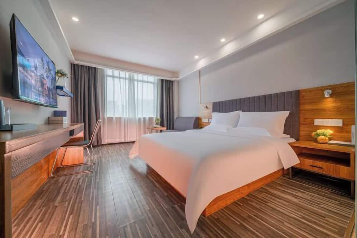 A modern hotel room with a large bed, a desk, a flat-screen TV, and a window with curtains.
