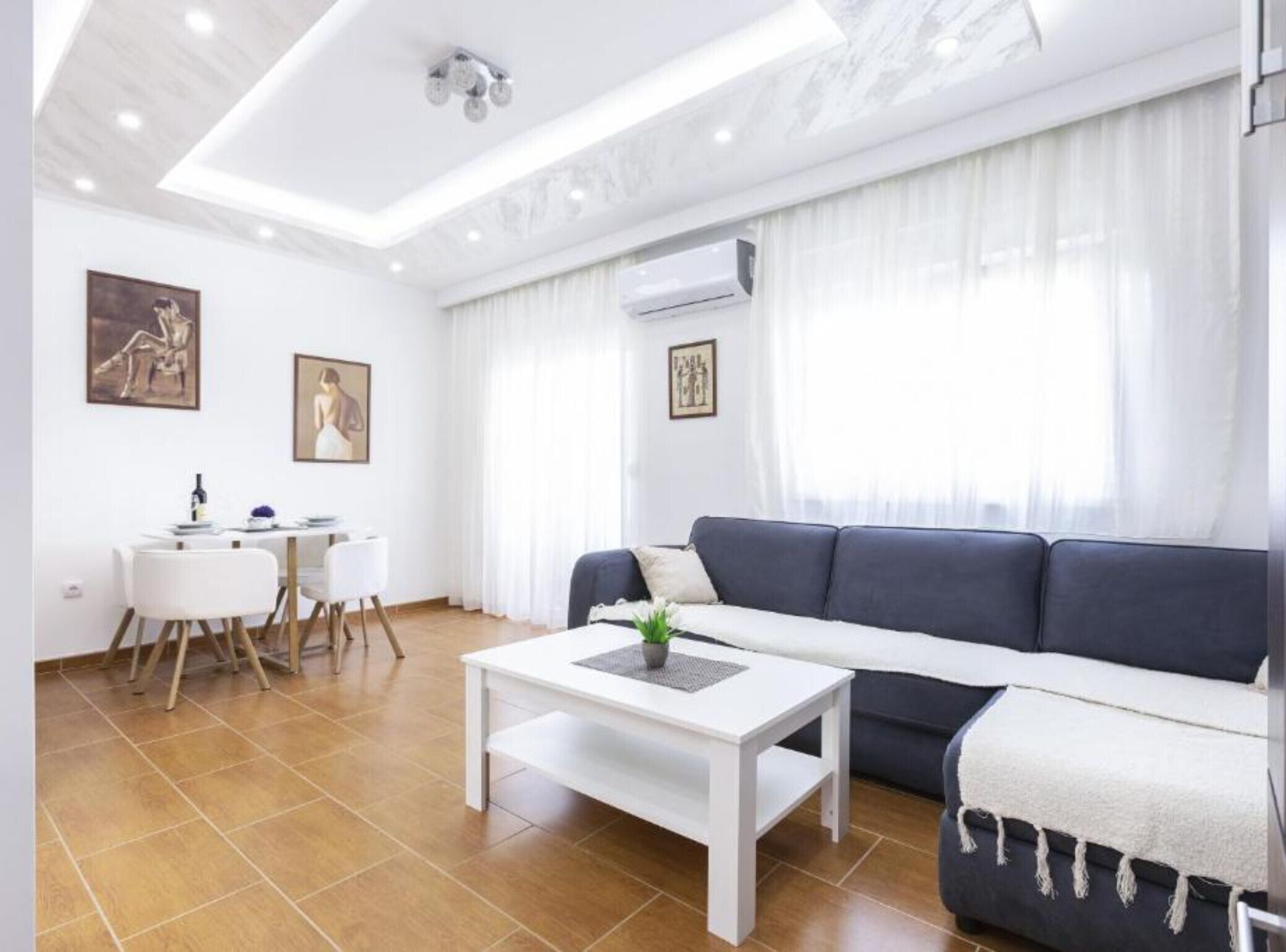 A modern living room with a sofa, a dining table with chairs, and artwork on the walls.