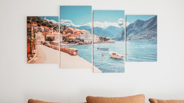 Un mur orné d’une œuvre d’art composée de quatre panneaux représentant une ville côtière avec ses bâtiments, une plage et des bateaux sur l’eau.