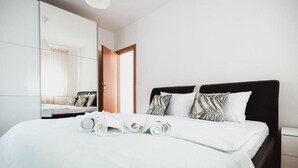 Un lit bien fait, avec des serviettes pliées en rouleau, une tête de lit noire et un miroir au mur.