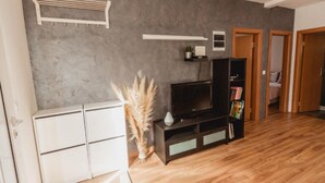 Un salon moderne avec un mur gris, un plancher en bois, un meuble blanc, un meuble noir pour l’équipement audiovisuel et une petite plante en pot.
