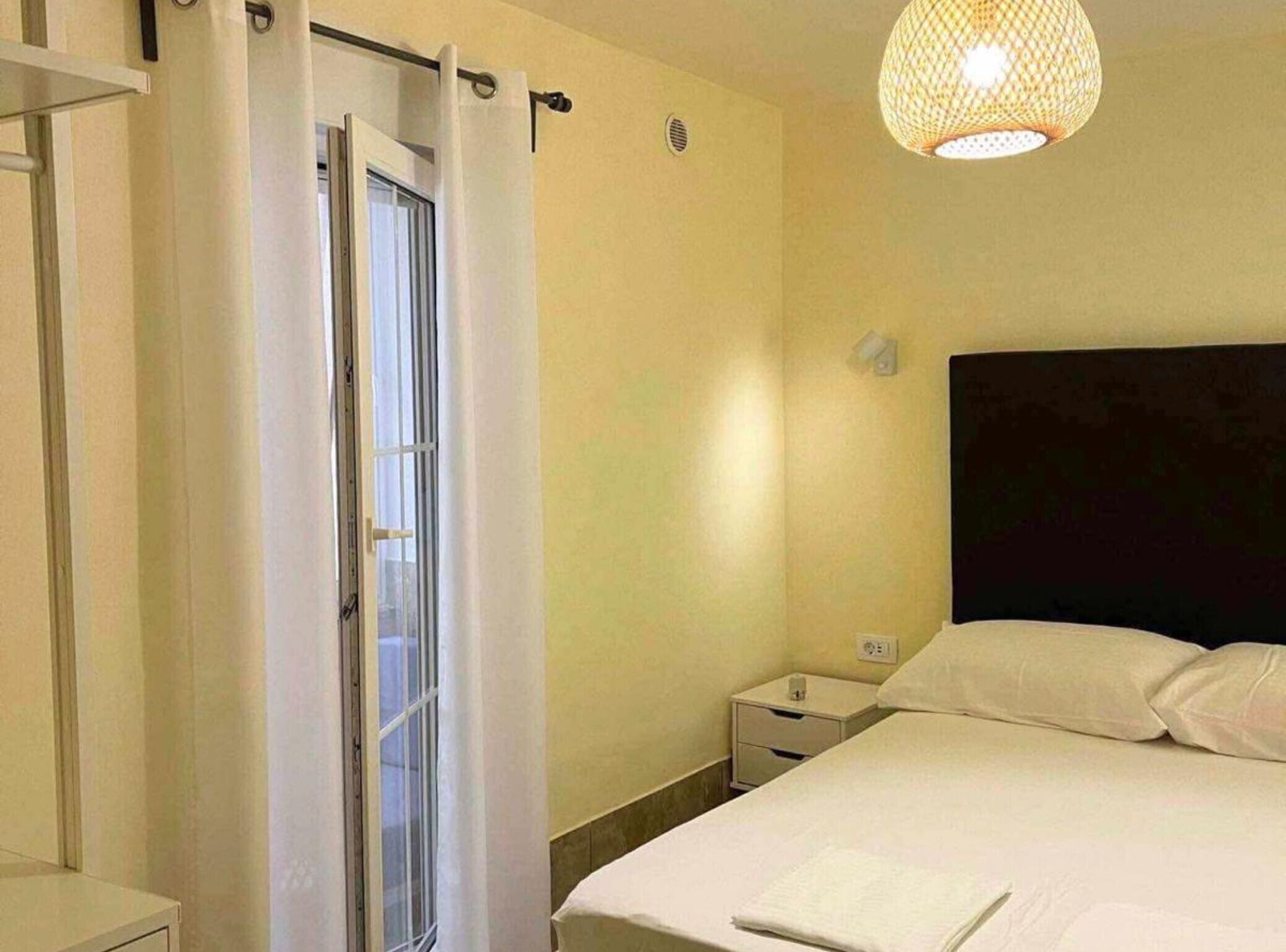 Een slaapkamer met een bed, nachtkastje, lamp en een raam met gordijnen.