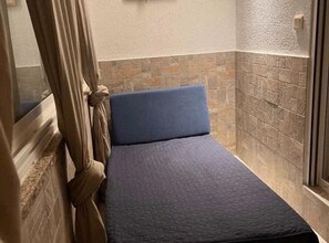 Cozy retreat with a single bed, tiled walls, and a window with curtains.