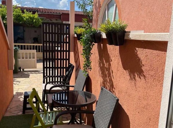 Relax in this serene outdoor seating area with a small table and four chairs, surrounded by lush greenery and a charming view.