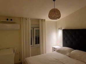 Un dormitorio con cama, mesita de noche, escritorio y ventana con cortinas.