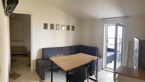 Ein kleiner, moderner Wohnraum mit einem Holztisch, zwei schwarzen Stühlen, einem grauen Sofa und einem Balkon mit einer Schiebetür.