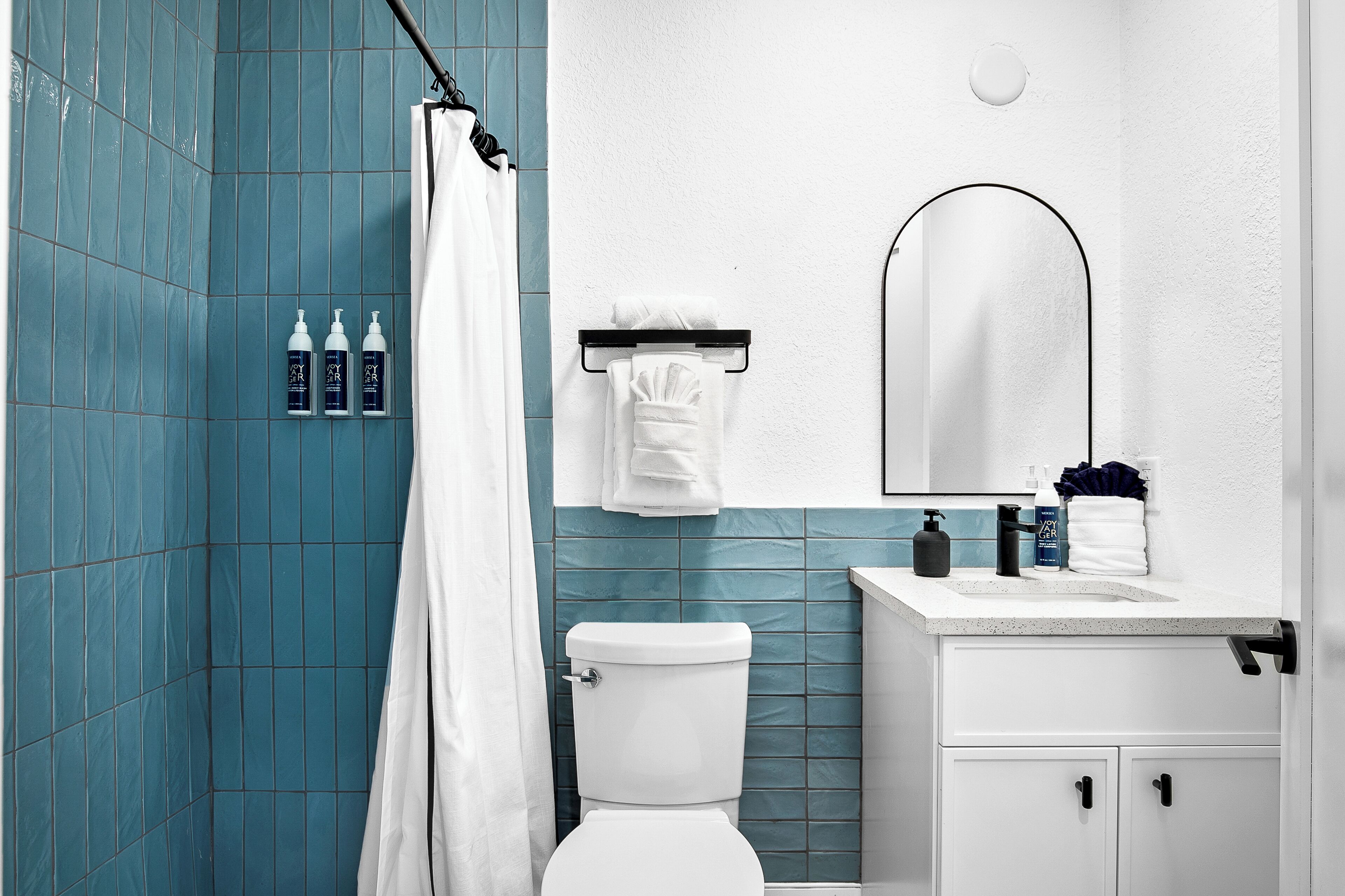 Une salle de bain avec des toilettes blanches, un rideau de douche et un lavabo avec des articles de toilette.