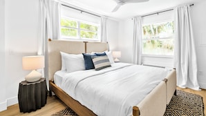 A bedroom with a bed, two bedside tables, a ceiling fan, and windows with curtains. - SeaSpray Resort (Siesta Key)