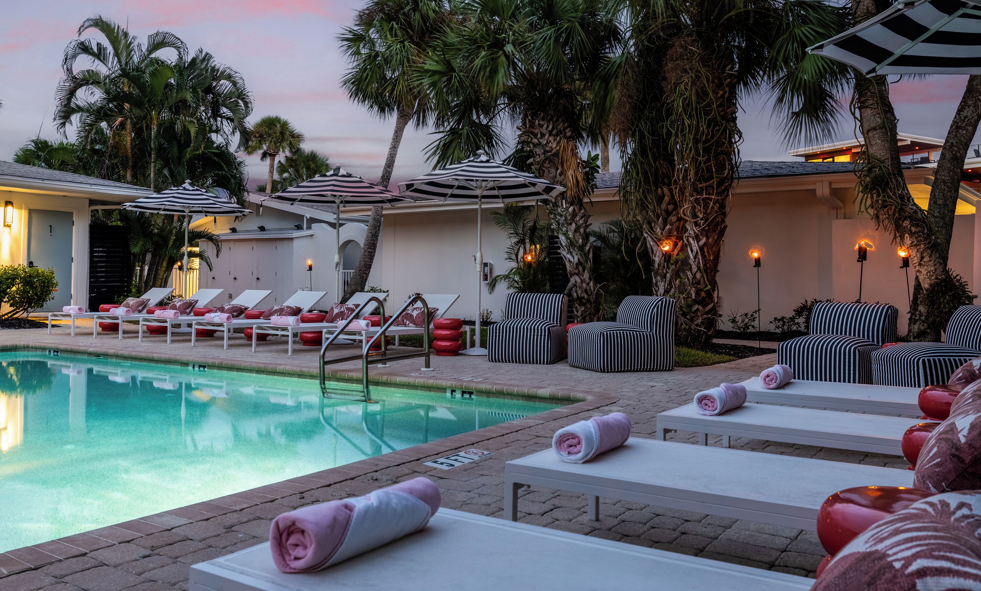 Un espace aménagé au bord de la piscine, avec des chaises longues, des parasols et une piscine.