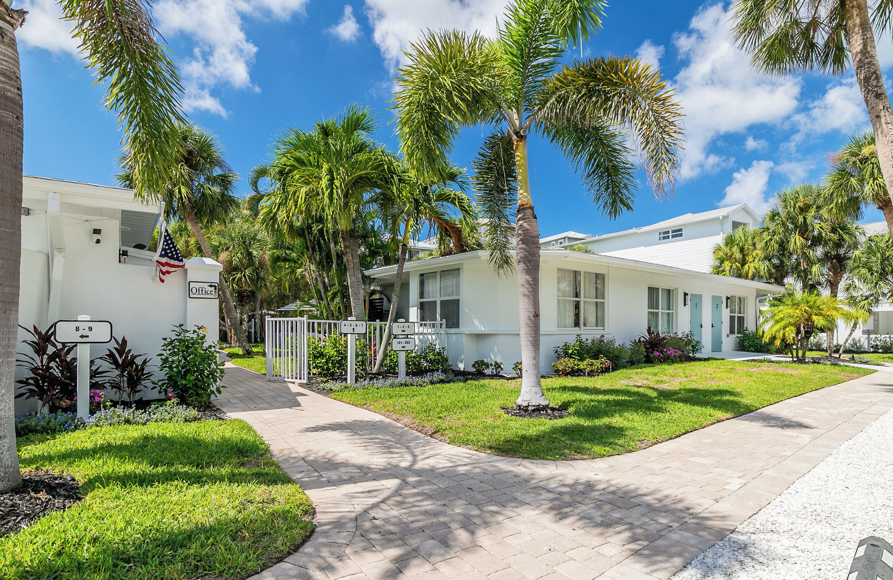 A residential area with a white building, palm trees, and a clear blue sky.