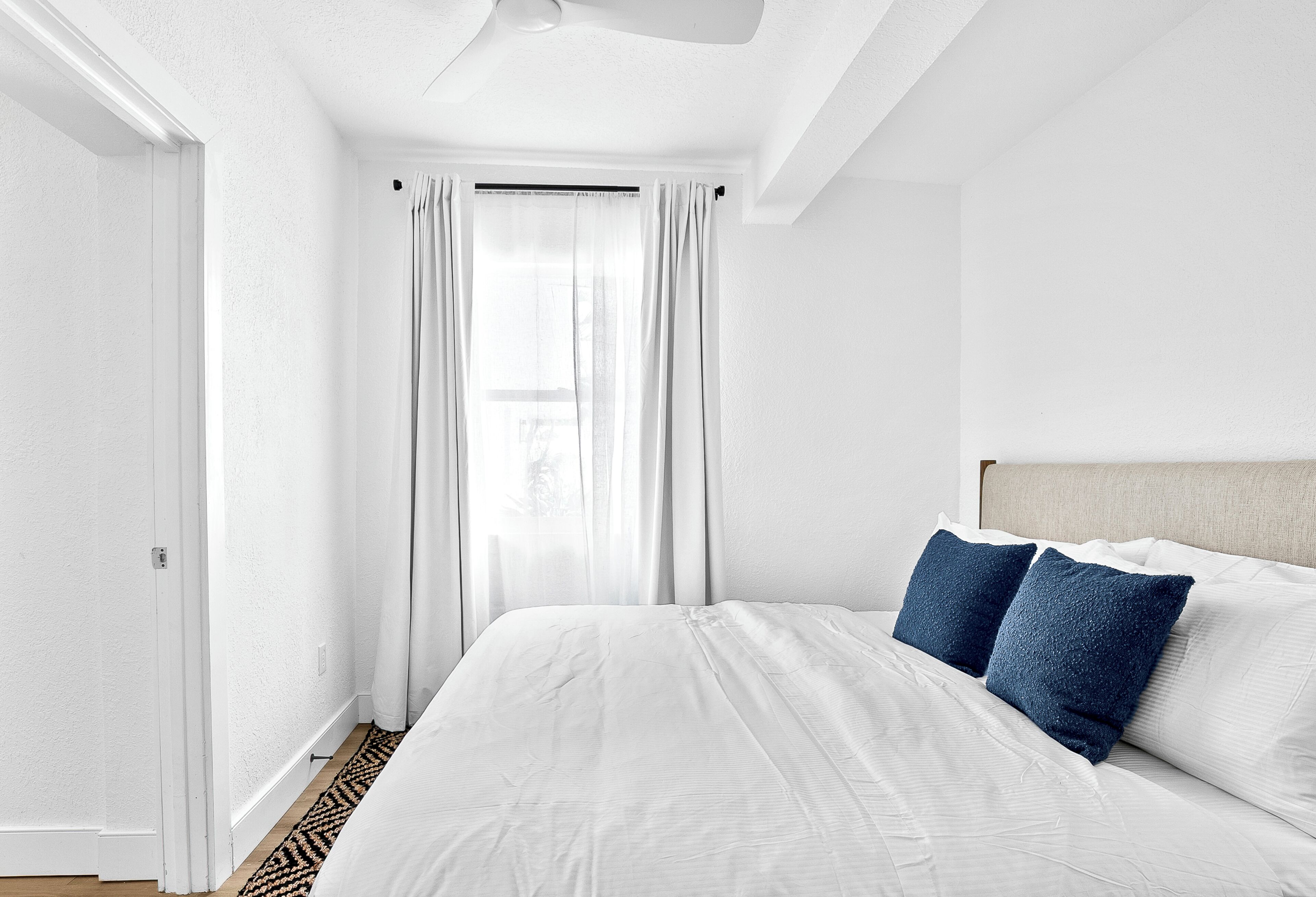 A bedroom with a bed, white curtains, and a ceiling fan.