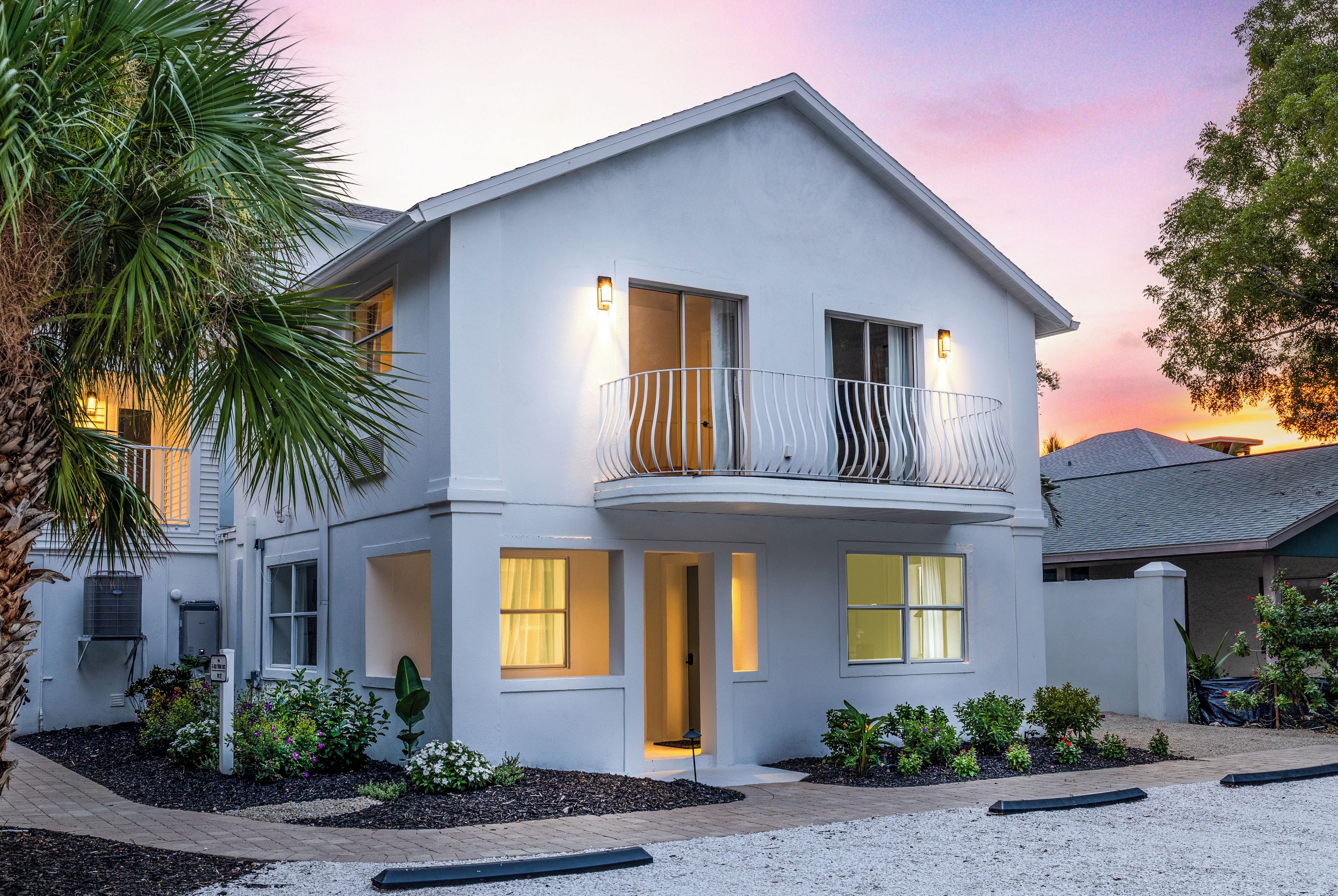 A two-story house with a balcony, a visible air conditioning unit, and a driveway leading to the entrance.