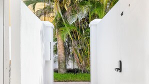 A narrow concrete pathway flanked by white walls, leading to a lush green area with palm trees and a small grassy patch. - SeaSpray Resort (Siesta Key)