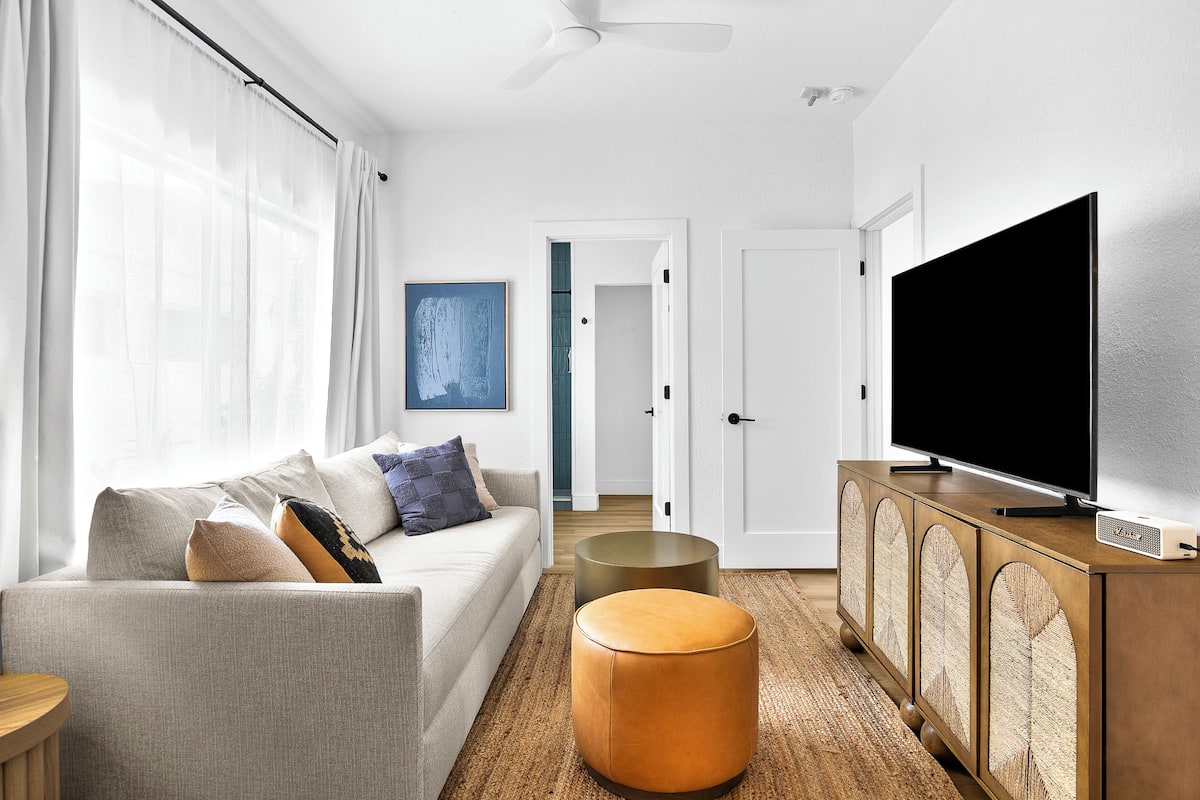A modern living room with a sofa, ottoman, TV, and a cabinet.