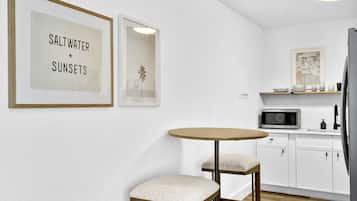 A modern kitchen with white cabinets, a microwave, and a round table with two chairs. There are framed pictures on the wall.