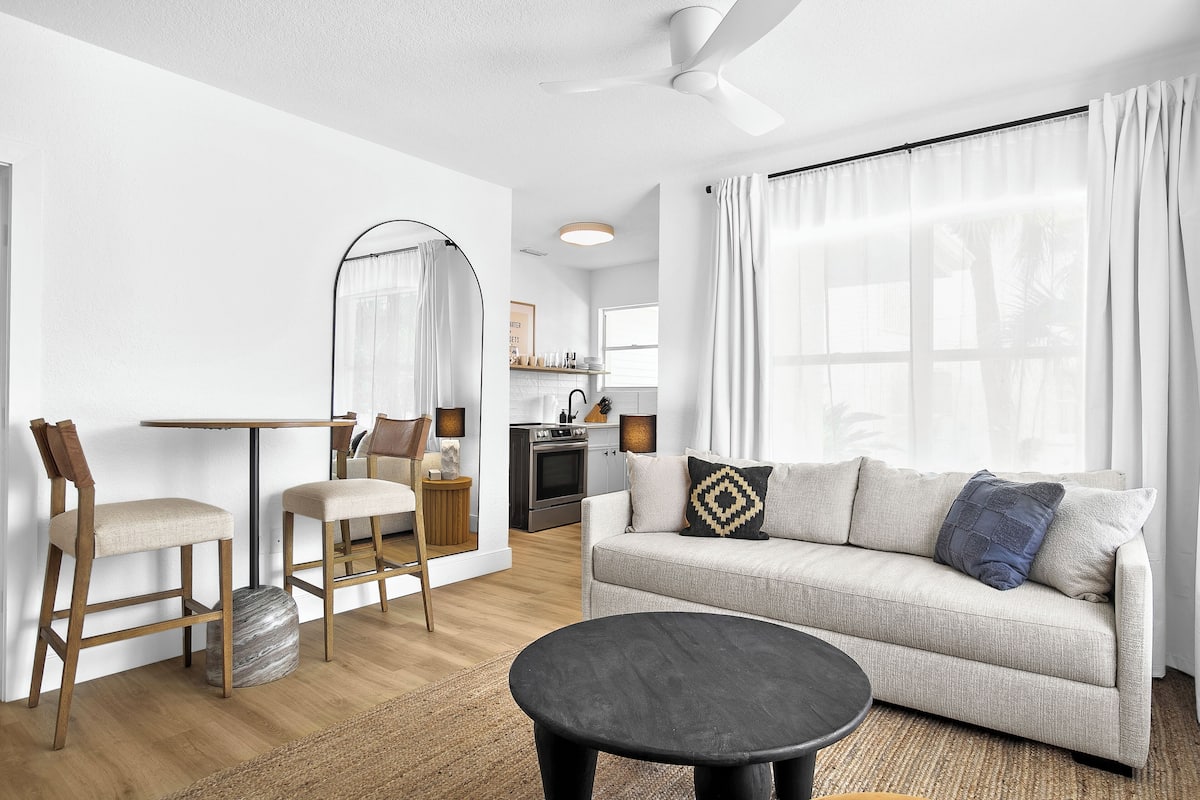 A modern living room with a sofa, two chairs, a round coffee table, and a dining table with chairs.
