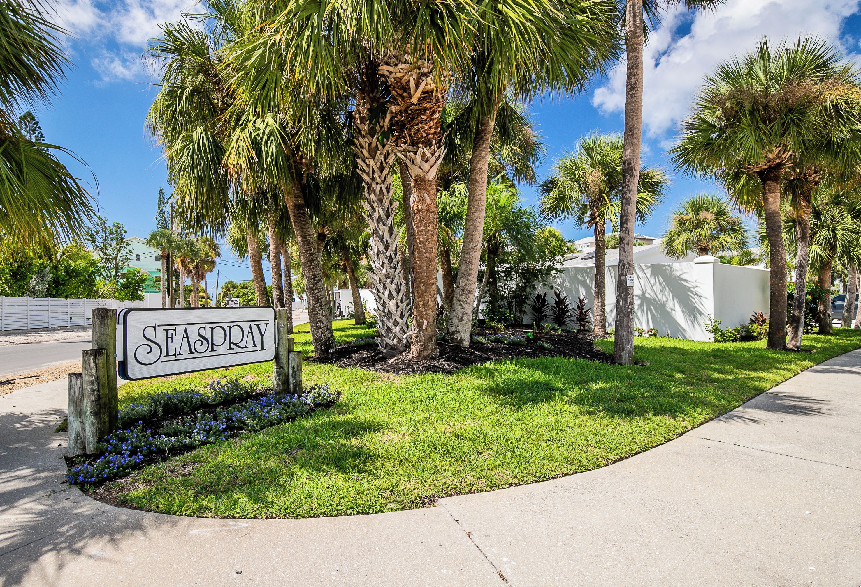 A sign for 'SEASPRAY' in a well-maintained area with palm trees and a clear sky.
